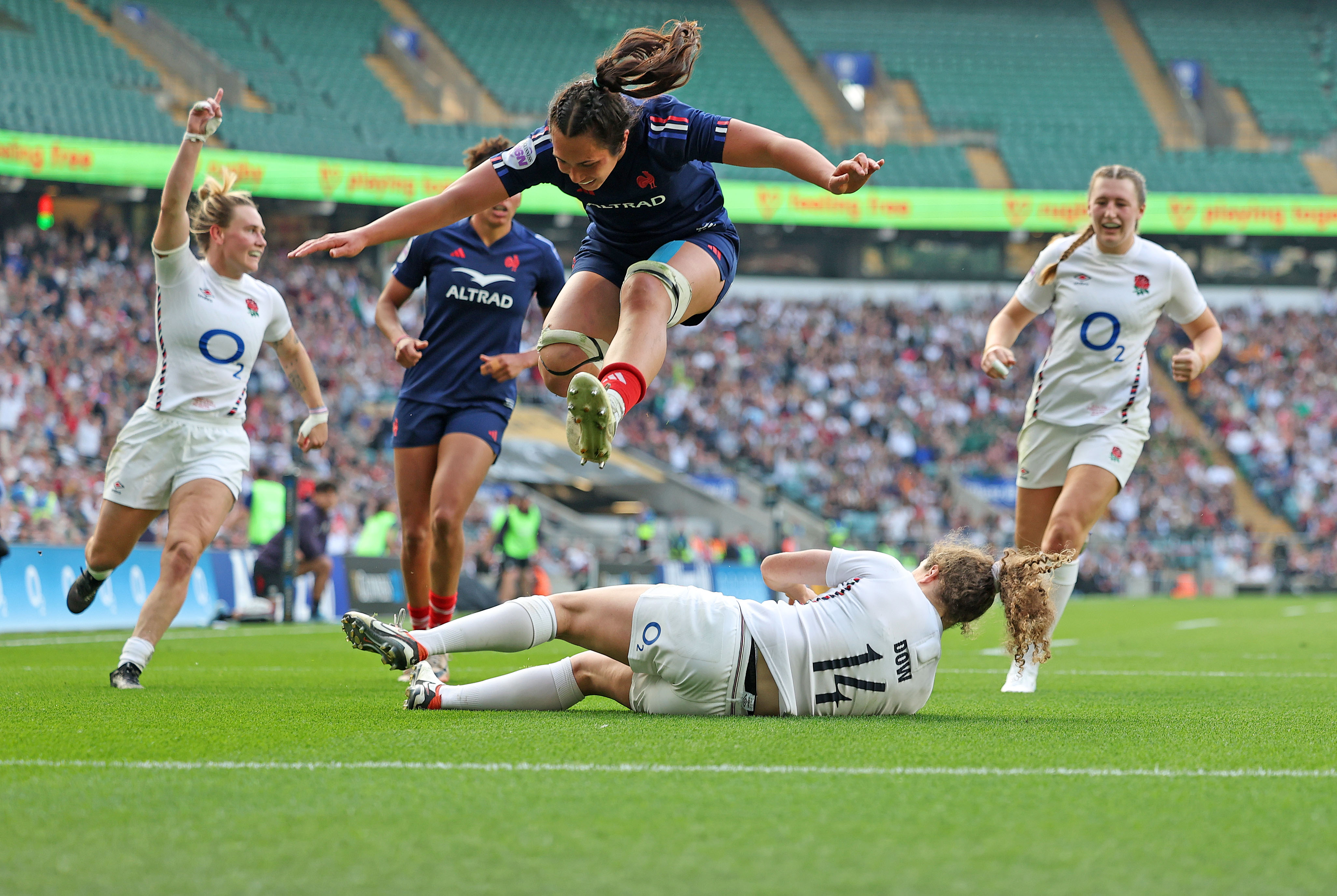 A rugby player leaps over a fallen opponent during a Women's Six Nations match between England and France.