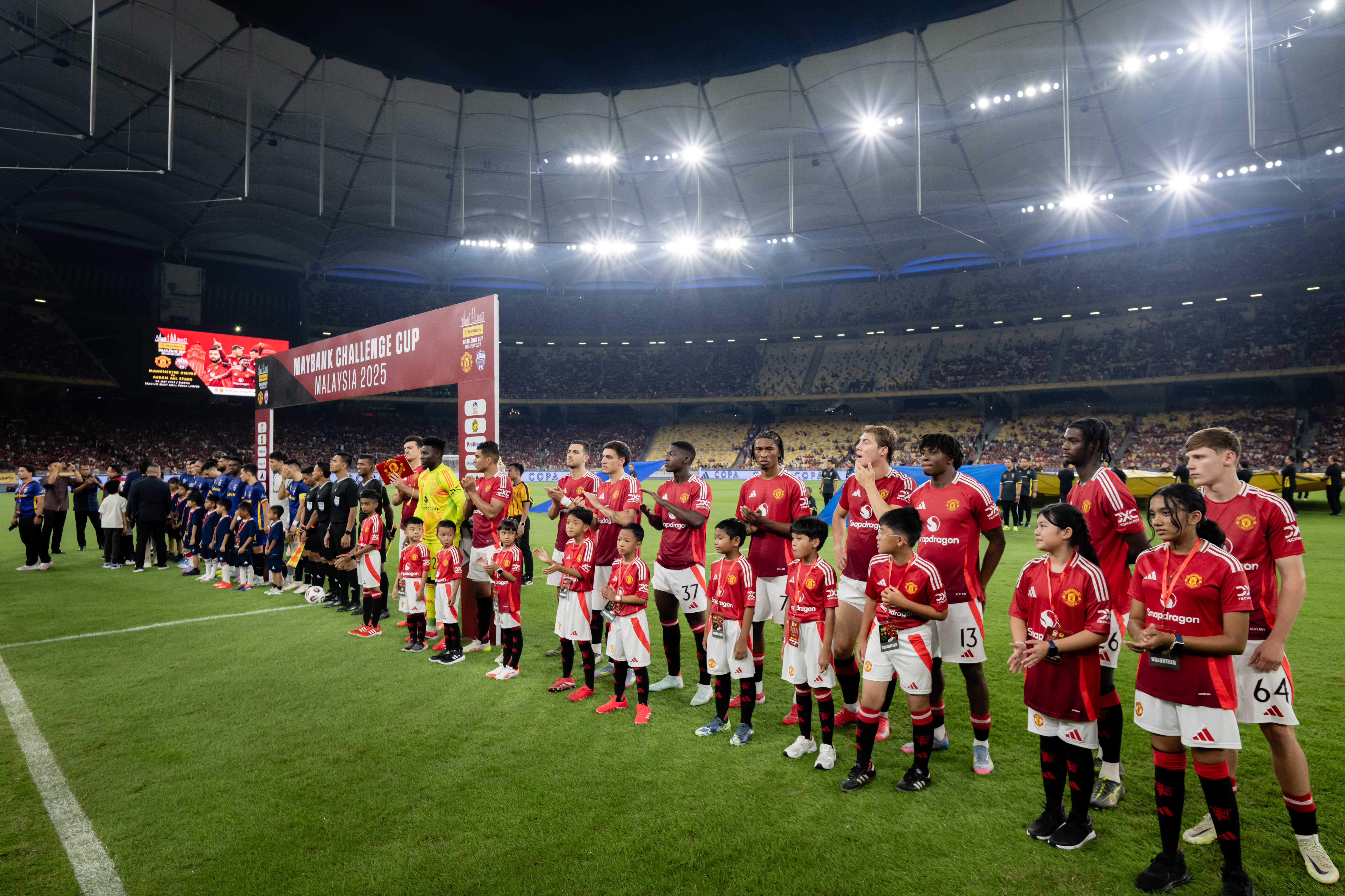 Manchester United players and young fans line up on the field before a soccer match.