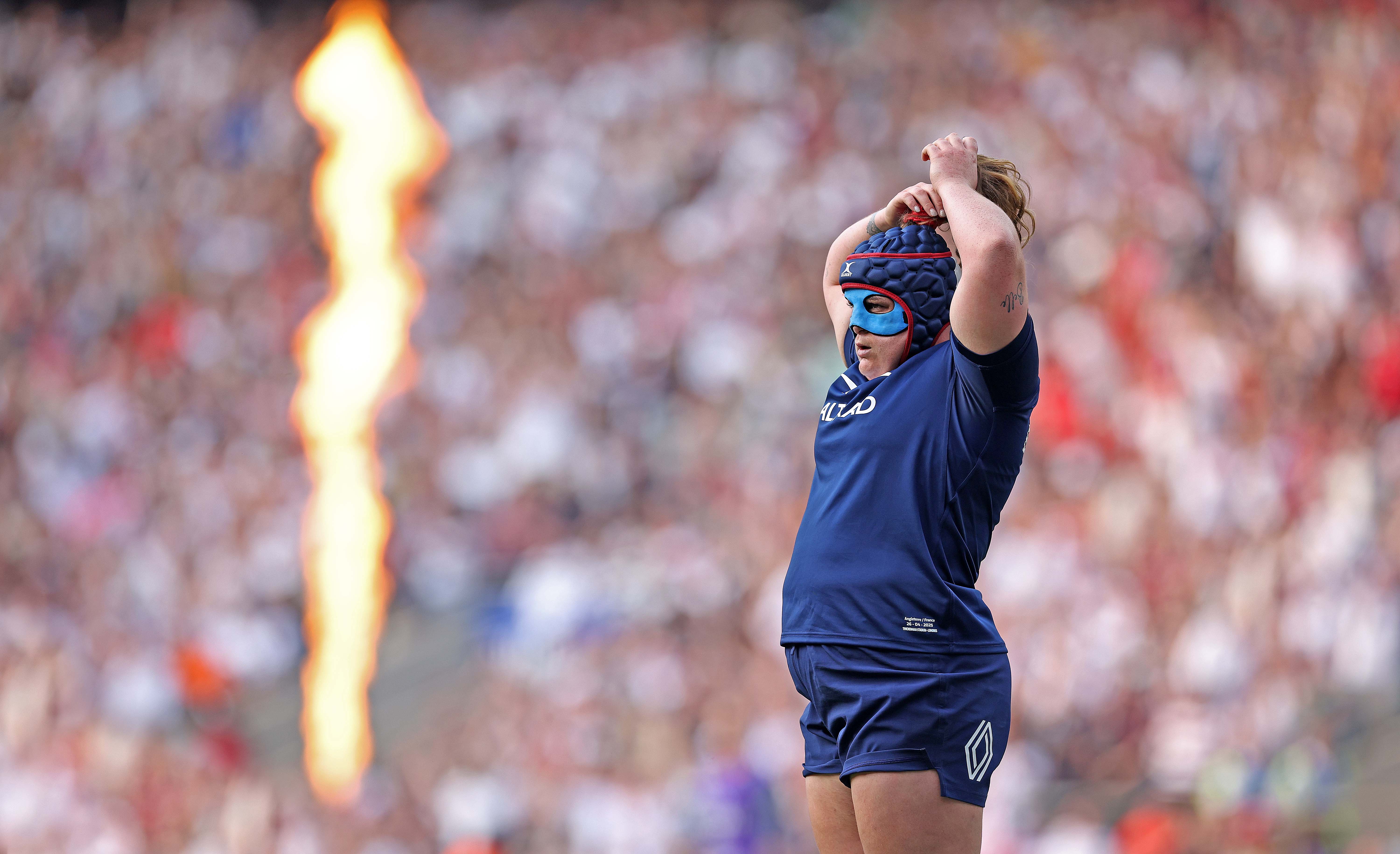 A female rugby player adjusts her protective headgear during a match.